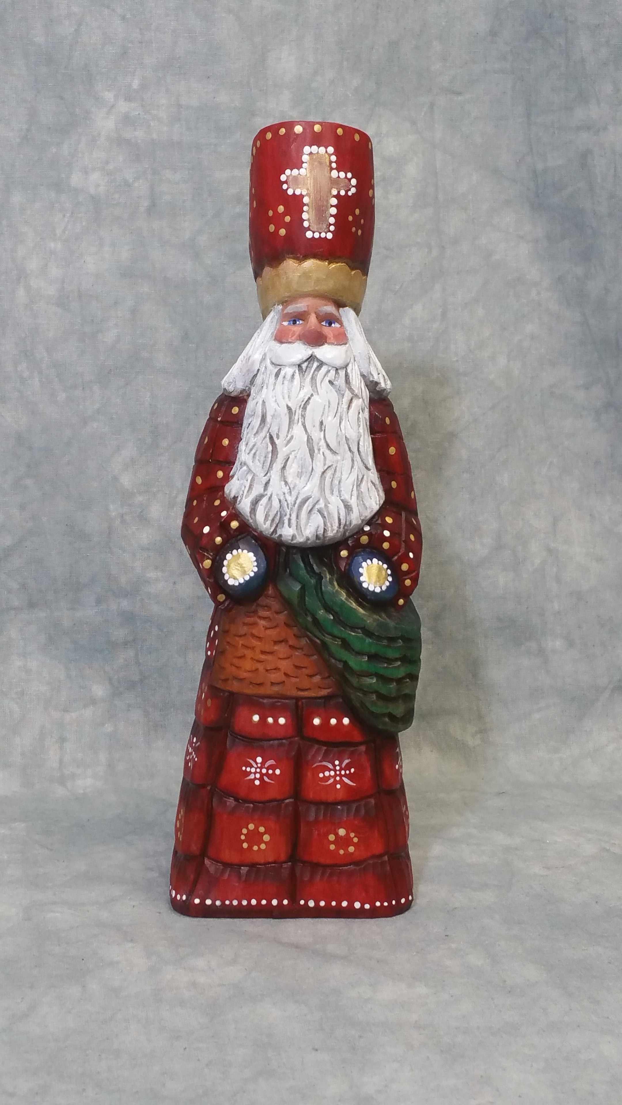 Father Christmas wood carving in red robe holding a basket and small figure, shown beside a wine bottle for scale